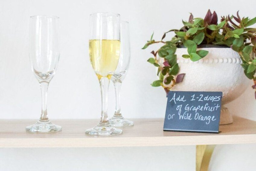 Two champagne flutes on a shelf, one filled with a yellow liquid, and a sign suggesting adding grapefruit or wild orange. 3