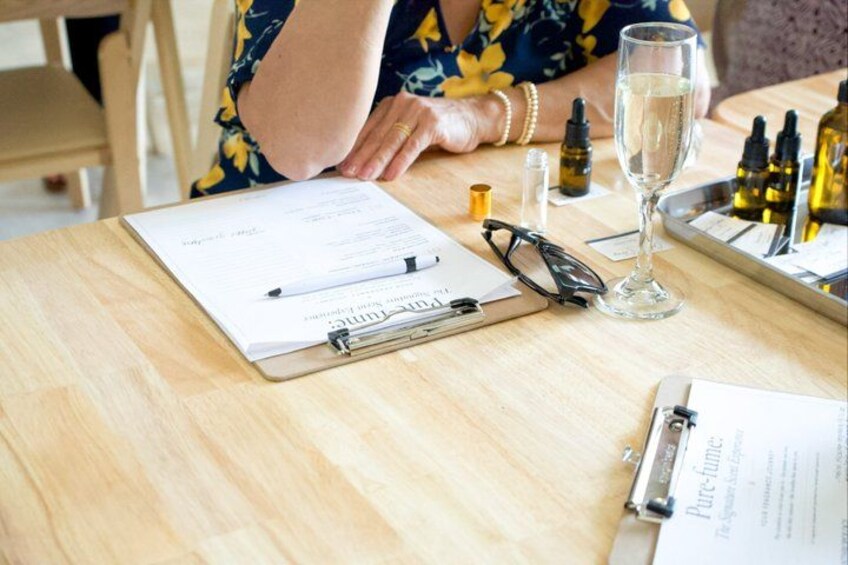 A wooden table with documents, a pen, a pair of glasses, a wine glass, and various bottles. 4