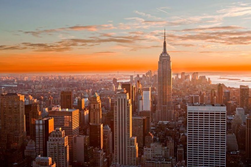 A cityscape with a prominent skyscraper, likely the Empire State Building, during sunset. 1