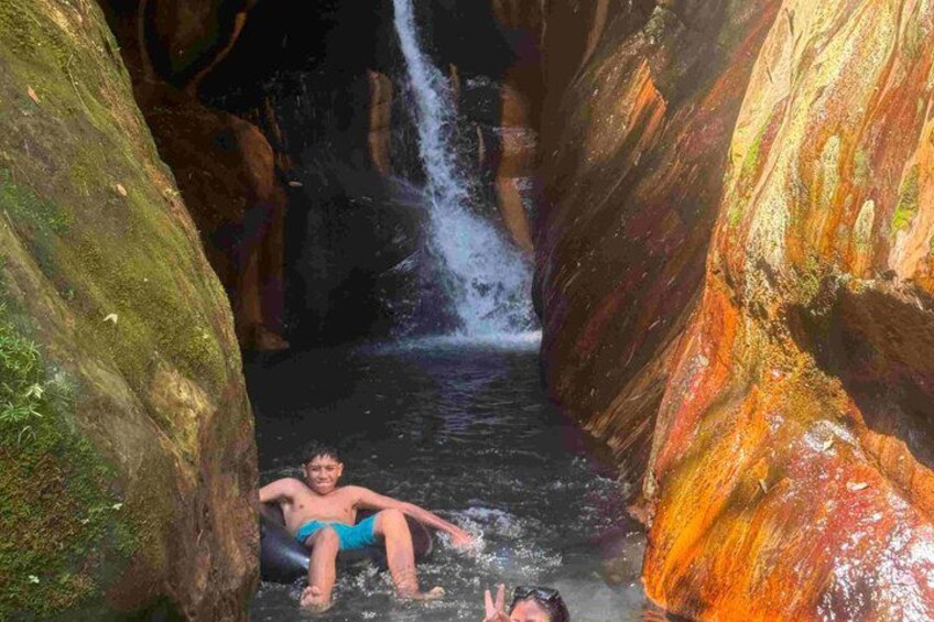 A person in blue swim trunks relaxing in a narrow water channel with a waterfall in the background. 3