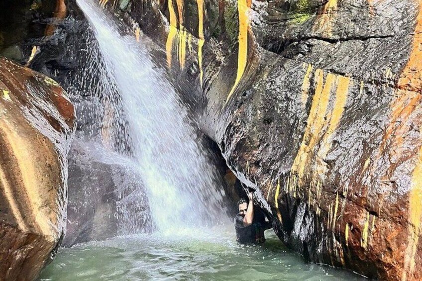 A waterfall in a rocky cave with yellowish streaks on the walls. 4