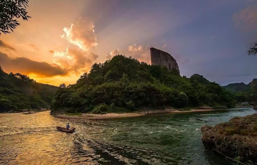 A river with a person in a boat, a rocky cliff, and dense greenery. 1
