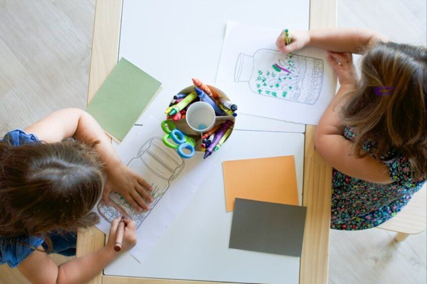 Two children drawing on paper with art supplies on a table. 4