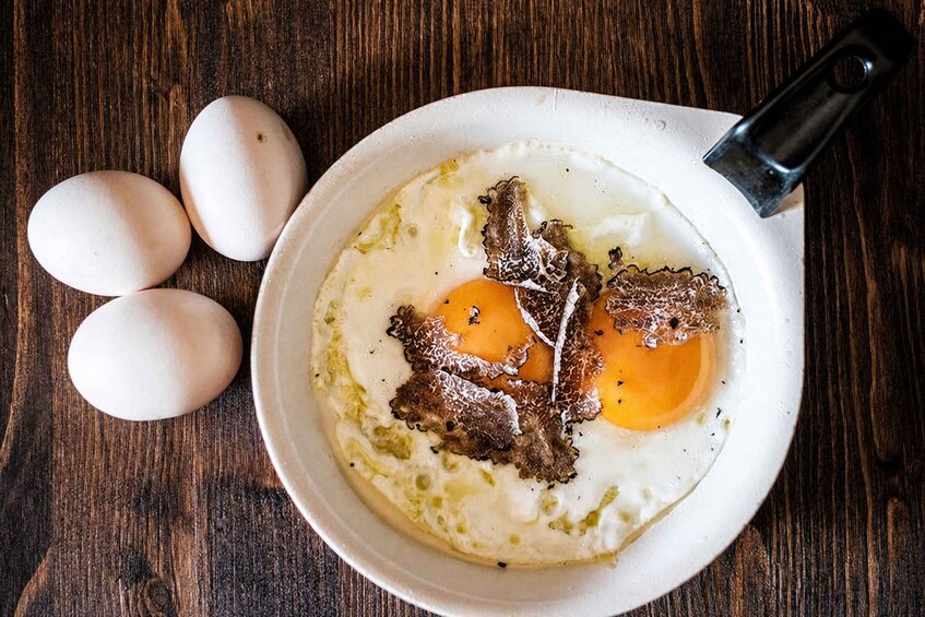 A plate with two fried eggs, some greens, and a piece of meat on a wooden table. 5