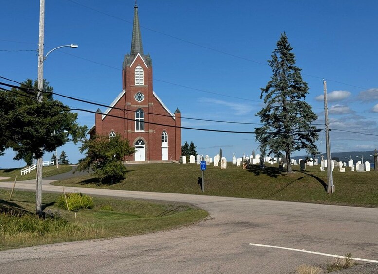 Eine rote Kirche mit einem Kirchturm, ein Friedhof mit weißen Grabsteinen und ein großer immergrüner Baum. 2