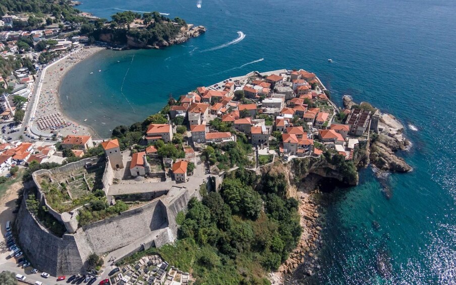 Eine Vogelperspektive einer Küstenstadt mit einer befestigten Burg, einem Strand und einem klaren, blauen Meer. 2