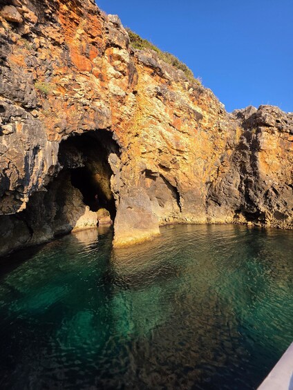 Eine steile Felsklippe mit einer Höhle und klarem Wasser. 3