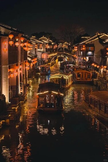 A traditional waterway with boats, illuminated buildings, and hanging lanterns. 1