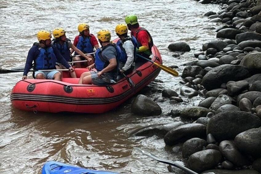 A group of people in a red inflatable raft navigating through a river with large rocks. 3