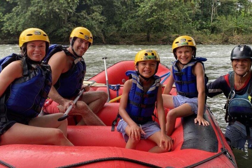 A group of people on a red raft with helmets, life jackets, and paddles. 2