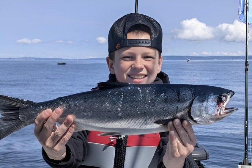 A person holding a fish by a body of water with a fishing rod in the background. 4