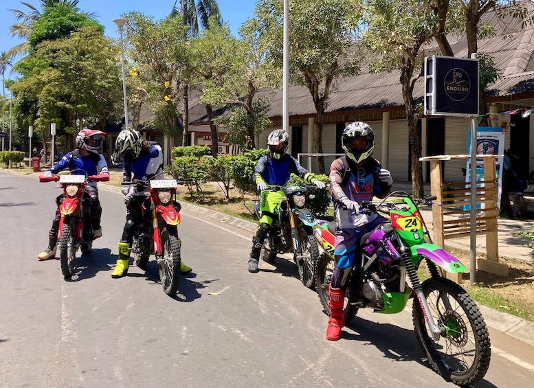 Four dirt bikes parked on a street with trees and a building in the background. 5