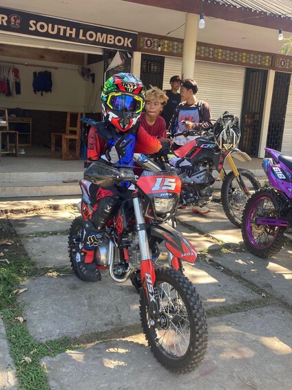 A dirt bike with the number 19 parked in front of a building with a sign that reads 'SOUTH LOMBOK'. 4
