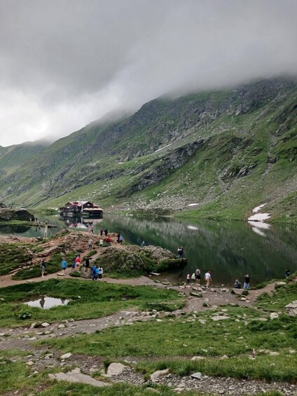 Eine Berglandschaft mit einem See, einer Holzhütte und Menschen, die sich dort aufhalten. 2