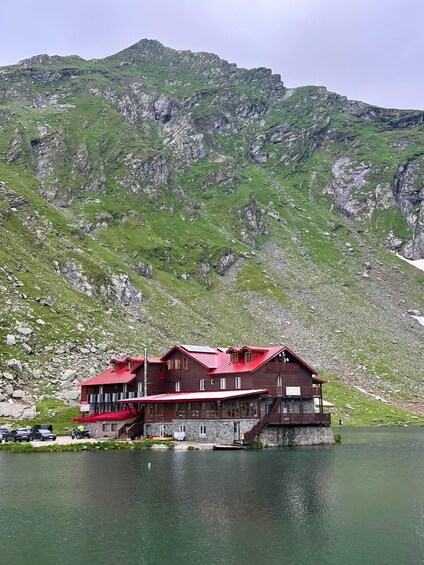 Eine Holzhütte mit rotem Dach am Seeufer, umgeben von Bergen. 3