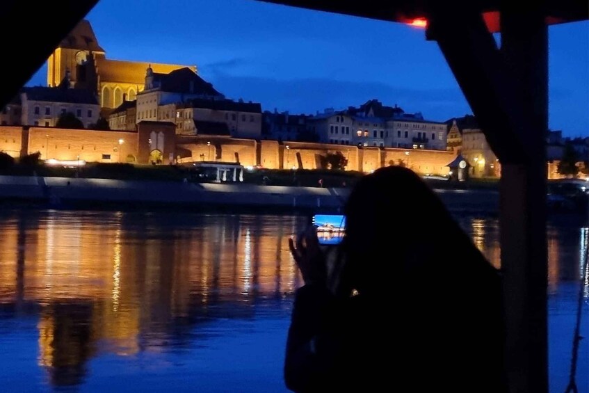 A person taking a photo of a lit-up historic building by a river at dusk. 5