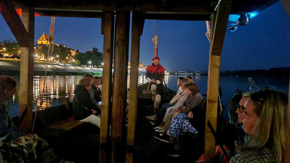 A group of people on a boat with a cityscape and a bridge in the background. 4