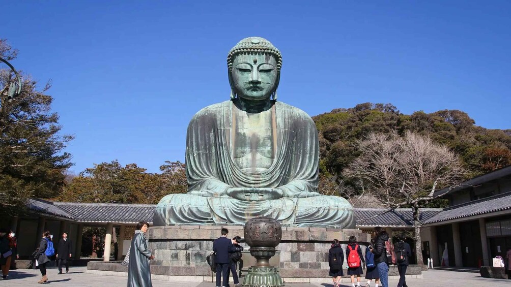 Una gran estatua de bronce de Buda en un patio de templo con visitantes a su alrededor. 1