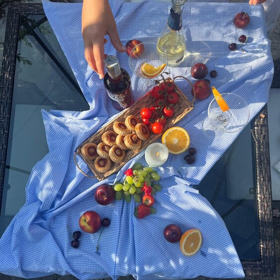 Ein Picknick mit kariertem Tischläufer, einer Korb voller Kirschtomaten, einer Weinflasche und verschiedenen Früchten und Gebäck. 1