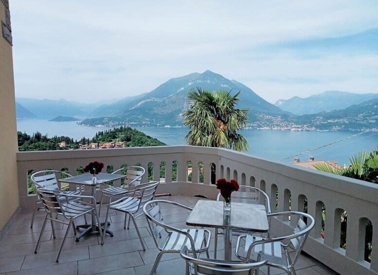 Eine Terrasse mit Metallstühlen und -tischen mit Blick auf einen See, im Hintergrund Berge. 5