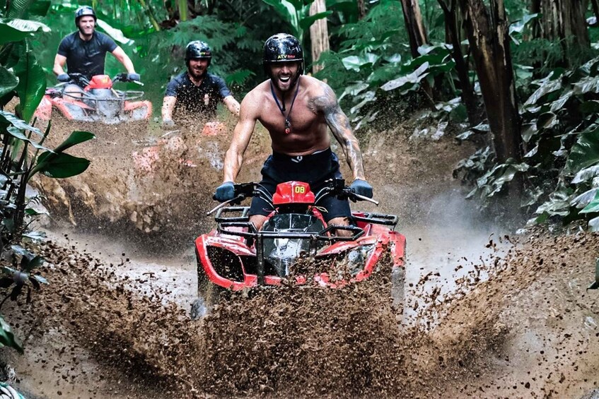 Eine Person fährt mit einem roten Quad durch einen schlammigen Waldweg. 5