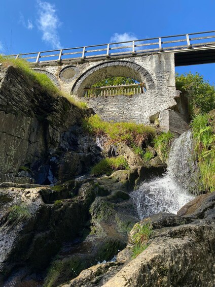 Un pont en pierre avec une rambarde en bois, une cascade et de la verdure. 3