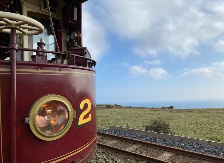 Une locomotive rouge portant le numéro 2, sur des rails, avec un champ verdoyant et un ciel dégagé en arrière-plan. 2