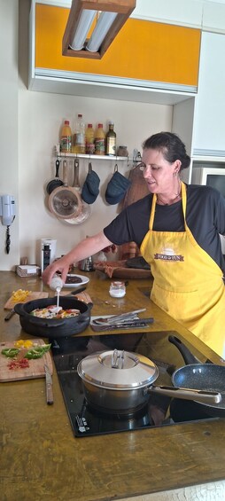 Une personne cuisine dans une cuisine, porte un tablier jaune, et divers ustensiles de cuisine et ingrédients sont disposés sur le plan de travail. 2