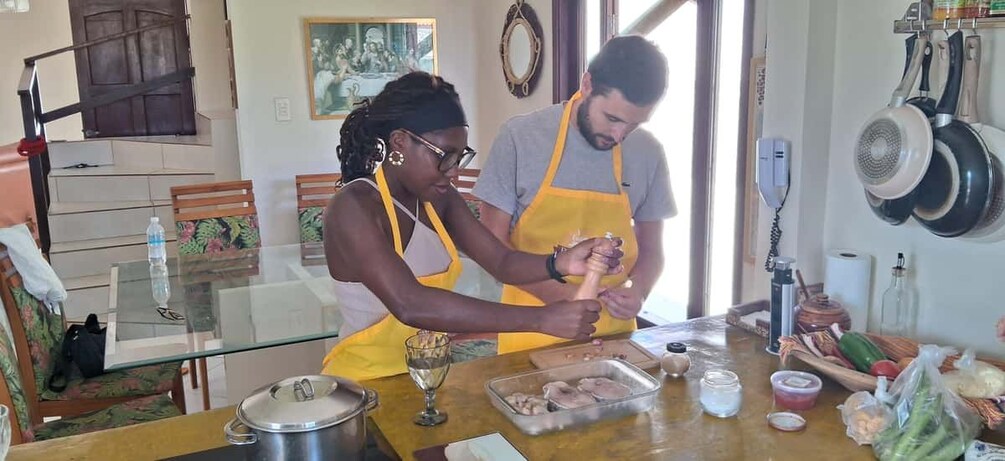 Deux personnes dans une cuisine, en train de préparer des aliments, avec une table remplie d’ingrédients et d’ustensiles de cuisine. 5