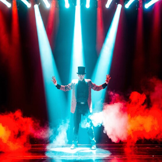Una persona en el escenario con los brazos extendidos, rodeada de luces y efectos de humo. 3