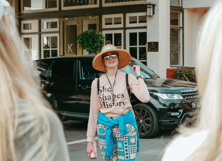 Une personne portant un chapeau de paille, un haut rose pâle et un pantalon à motifs, se tient devant un Range Rover noir. 2
