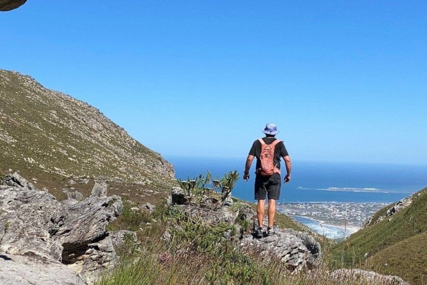 A person hiking on a rocky path with a view of the ocean and a distant city. 1