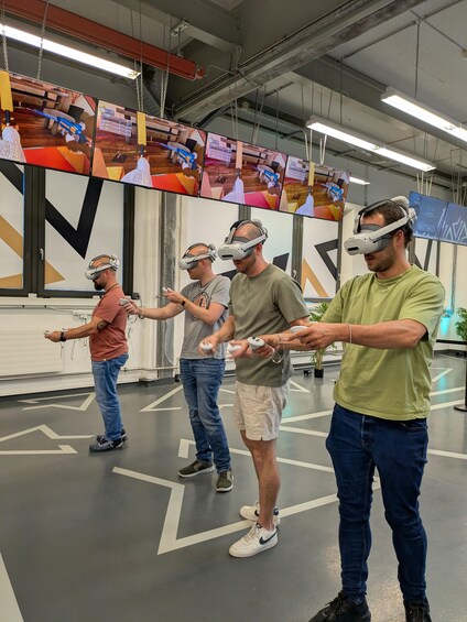 Four people wearing VR headsets in a room with a modern design, including a large geometric wall art piece and a ceiling with exposed beams and lighting fixtures. 1