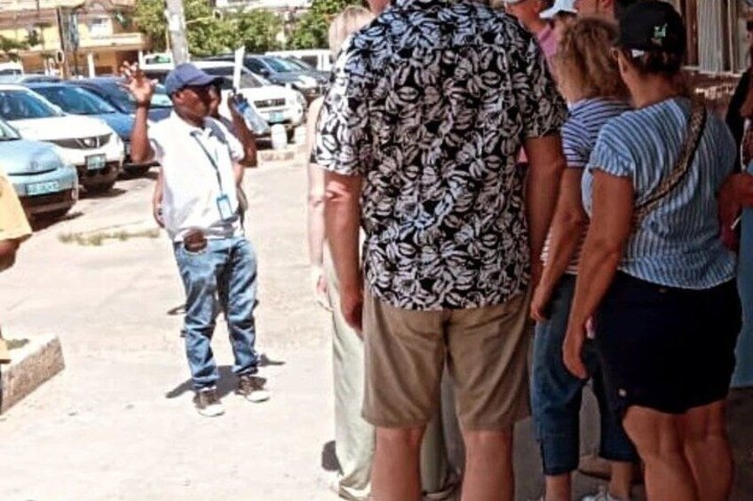 A group of people standing on a sidewalk, a man in a patterned shirt, and parked cars in the background. 4