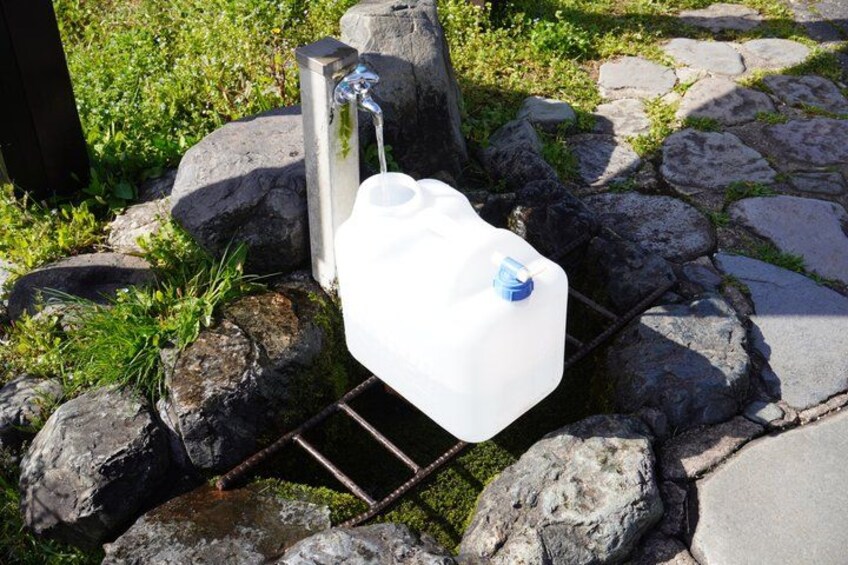 A water spigot connected to a white plastic container on a stone surface. 4