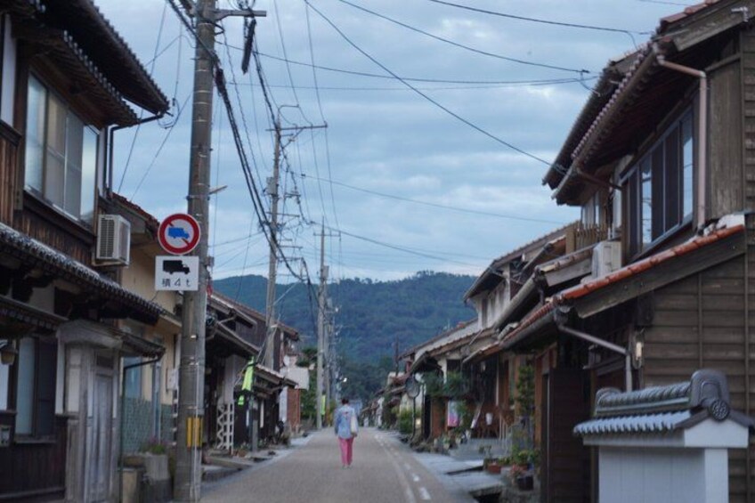 A narrow street lined with traditional wooden buildings, a no-parking sign, and power lines overhead. 5