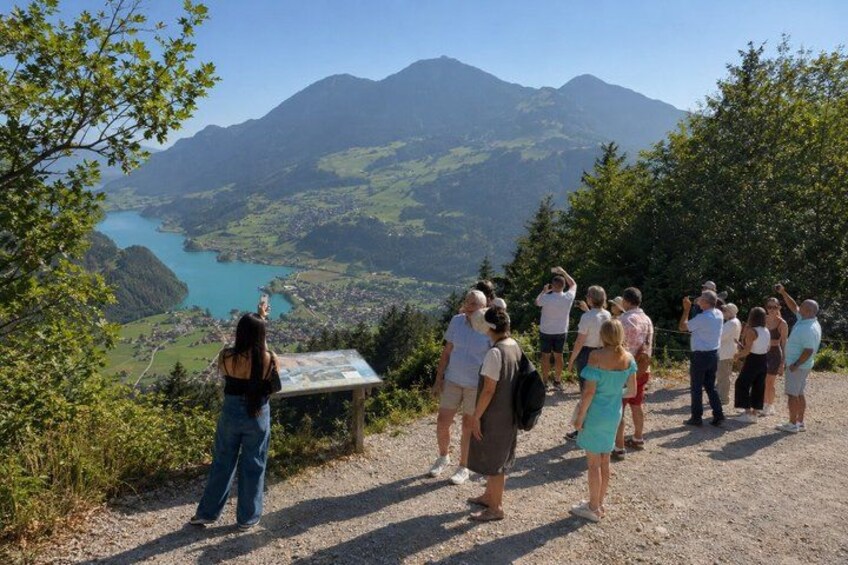 A group of people standing on a gravel path overlooking a lake and mountains. 3