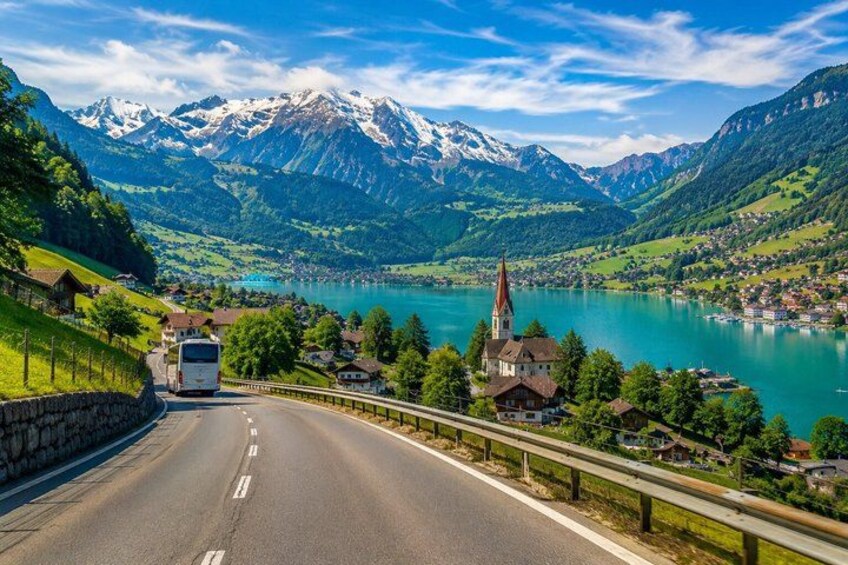 A road with a bus, a church, and a lake surrounded by mountains. 1