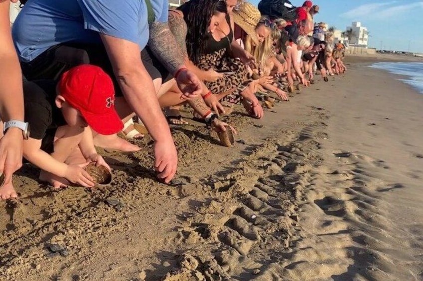 A group of people on a sandy beach, some bending over to interact with the sand. 1