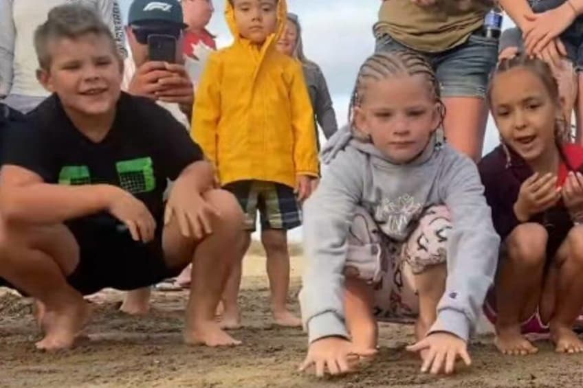 Children crouching on a sandy surface, possibly at a beach or outdoor event. 2