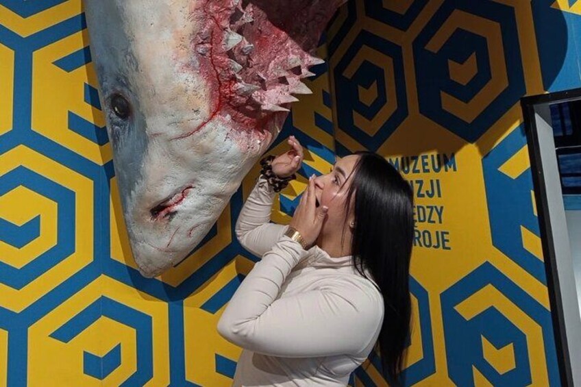 A person in front of a large shark sculpture with a geometric patterned wall in the background. 5