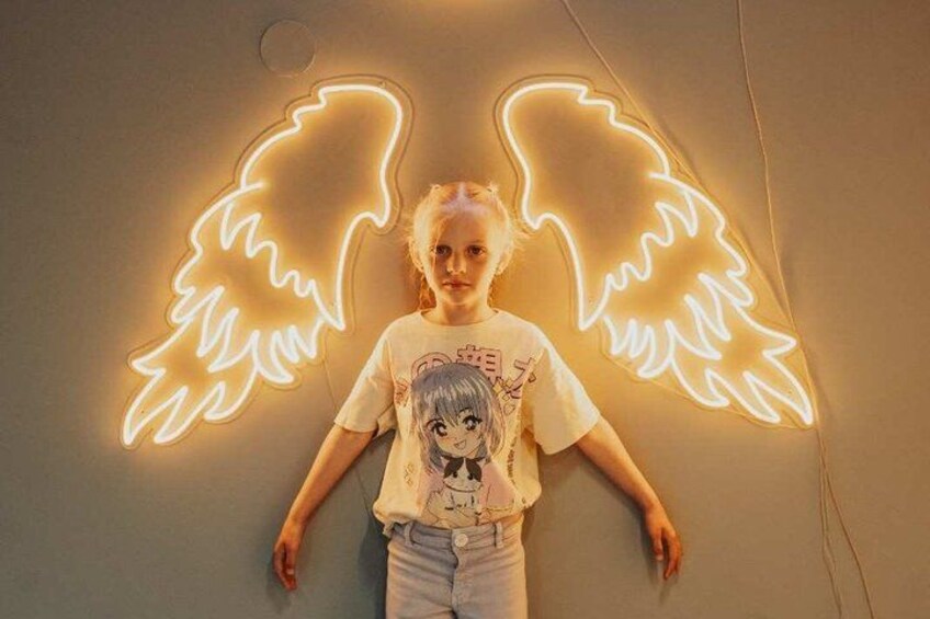 A person standing in front of a neon light shaped like wings. 2