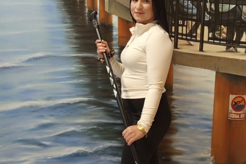 A person holding a paddle in front of a mural depicting a body of water. 4