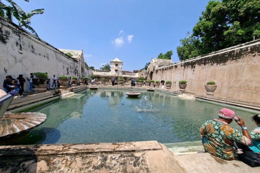 A historical site with a large central pool, stone walls, and visitors. 5