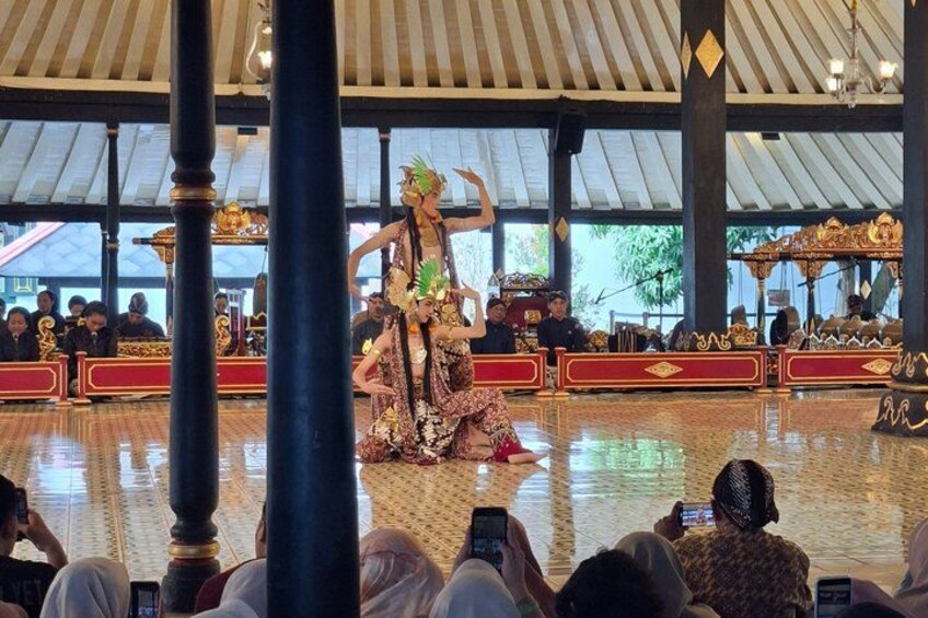 A traditional dance performance in a covered pavilion with ornate decorations and a polished floor. 4