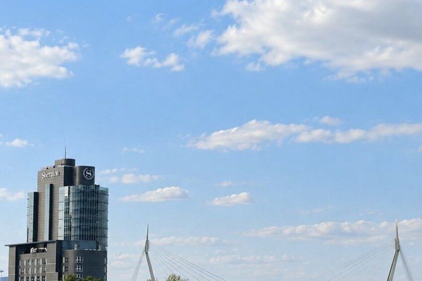 A modern building with a glass facade and a bridge with cables in the background. 2