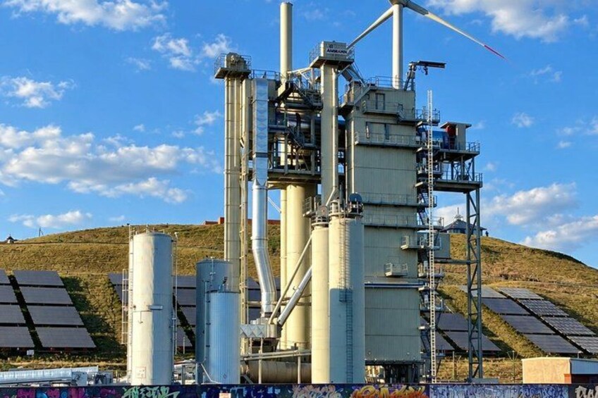 A wind turbine, solar panels, and industrial structures on a hill. 3