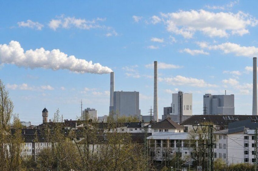 Industrial buildings with smokestacks, a clear sky, and some trees in the foreground. 5