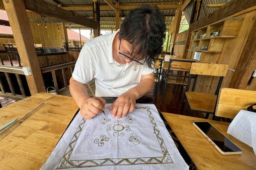 A person drawing on a table with a patterned cloth. 3