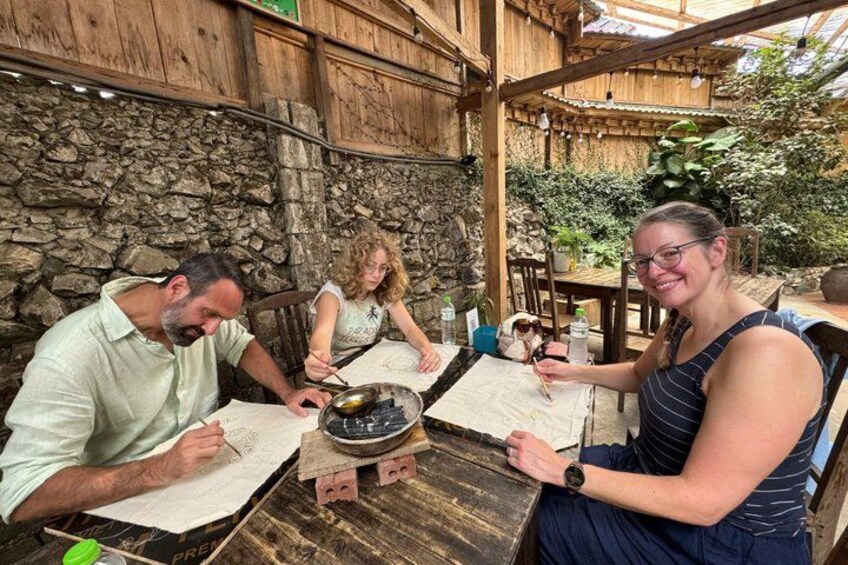 Three people engaged in a cooking activity outdoors, with a rustic wooden table and stone wall in the background. 4